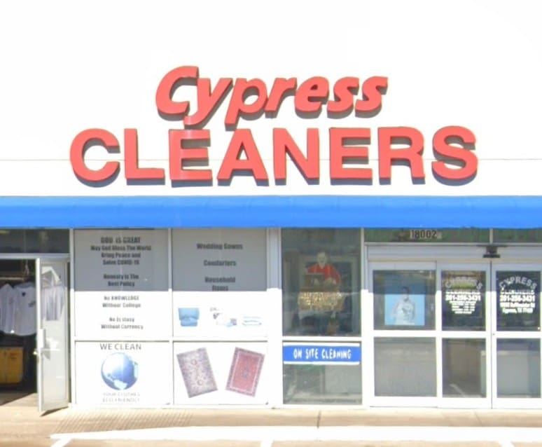 The storefront of Cypress Cleaners, featuring large red signage, a blue awning, and posters advertising cleaning and laundry services in the windows.
