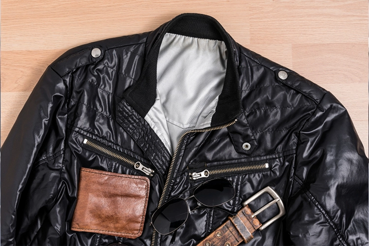 A black leather jacket with zippered pockets, a brown leather wallet, sunglasses, and a brown belt displayed on a wooden surface.