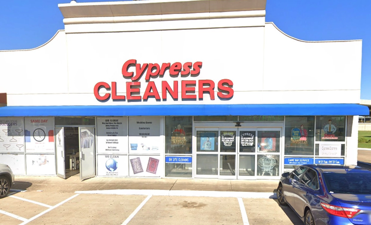 Storefront of Cypress Cleaners with large red signage, a blue awning, and a parked blue car in front on a sunny day.